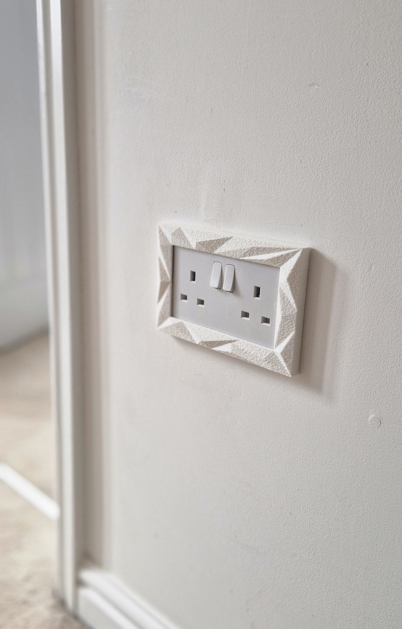 May include: White electrical outlet with two switches and three plugs, framed in a white geometric design.