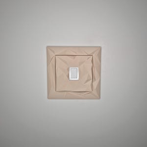 May include: A light beige, geometric-patterned light switch cover with a rectangular, silver-colored switch. The cover has a square shape with a textured, folded paper-like design. The switch is centered within the cover.