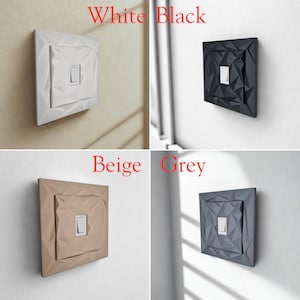 May include: Four decorative light switch covers in white, black, beige, and grey. Each cover has a geometric, faceted design around a rectangular switch. The words "White", "Black", "Beige", and "Grey" are written above each switch.