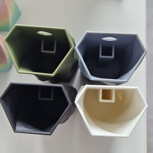 May include: Four hexagonal shaped containers with a hole in the top. The containers are in shades of green, grey, and white.