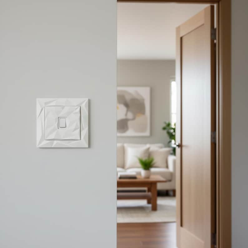 May include: A white, geometric light switch mounted on a light gray wall. The switch has a square, textured face with a smaller square in the center. The design features a series of angled lines, creating a modern, minimalist aesthetic. The switch is near an open wooden door.