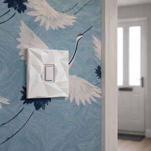 White geometric light switch cover installed in a modern hallway.