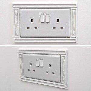 May include: A white double electrical wall outlet with two switches, featuring a decorative rectangular frame with textured side panels. The outlet has a standard three-prong configuration for each socket, presented in both a front and angled view.