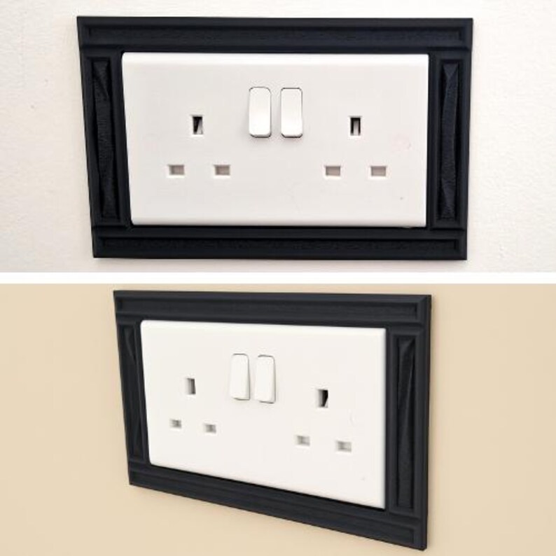 May include: A white double electrical wall outlet with two switches, framed by a rectangular black decorative cover plate. The frame features a textured, molded border design that surrounds the standard rectangular white plastic socket unit.