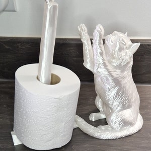 May include: White ceramic toilet paper holder shaped like a cat with a bird on top. The cat is sitting up with its paws raised and its tail curled around the toilet paper roll.