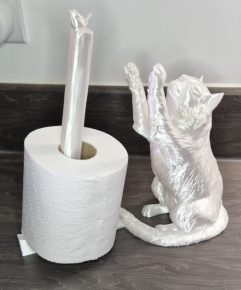 May include: White ceramic toilet paper holder shaped like a cat with a bird on top. The cat is sitting up with its paws raised and its tail curled around the toilet paper roll.