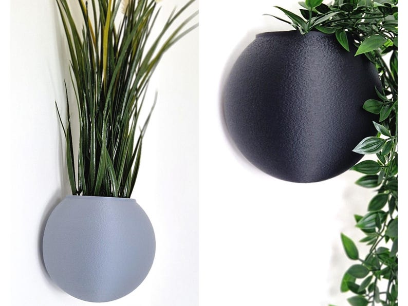 May include: Two round wall planters, one gray and one black, with a plant in each. The gray planter has a green plant with long, thin leaves. The black planter has a green plant with small, round leaves.