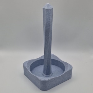 Puede incluir: Un porta rollos de papel de cer&aacute;mica gris, de forma geom&eacute;trica, con una base cuadrada y una alta aguja puntiaguda.