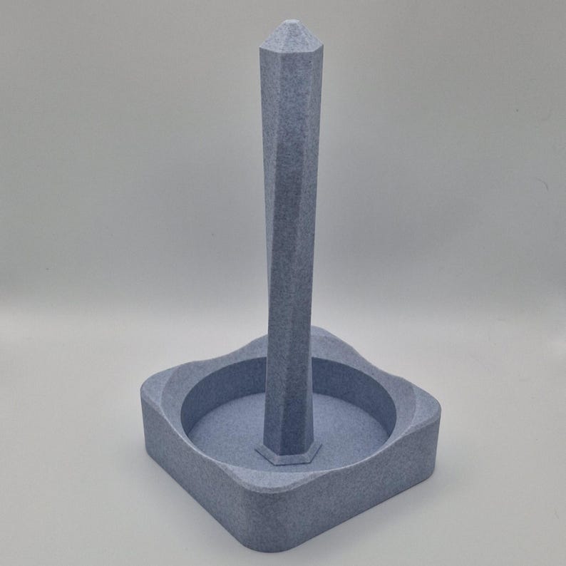 Puede incluir: Un porta rollos de papel de cer&aacute;mica gris, de forma geom&eacute;trica, con una base cuadrada y una alta aguja puntiaguda.