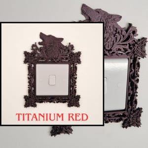 May include: A decorative, dark red light switch cover with a wolf head design. The frame has an ornate, floral pattern and the text "TITANIUM RED" is visible below the switch. The switch cover is mounted on a white wall.