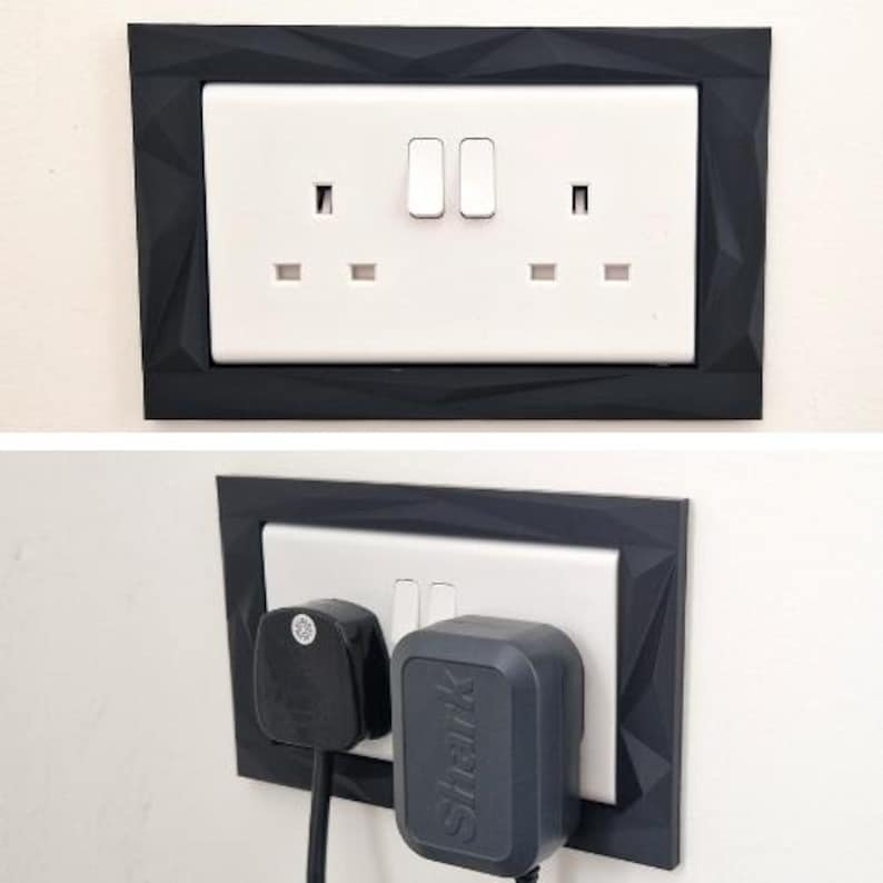 Może przedstawiać: Białe podw&oacute;jne gniazdko elektryczne z czarną geometryczną ramką o fasetowanej, kanciastej fakturze powierzchni. Gniazdko zawiera dwa przełączniki i dwa otwory, z włożoną czarną wtyczką oraz szarą wtyczką marki Shark.