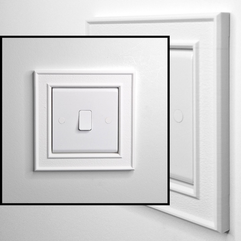 May include: A white square light switch featuring a central rocker toggle mechanism, surrounded by a decorative square frame with beveled edges. The switch plate has a smooth finish and includes two small circular screw covers on either side.