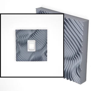 May include: A square light switch cover plate featuring a grey, three-dimensional wavy, rippled texture across its surface. The cover plate has a centered rectangular cutout containing a standard white rocker-style light switch toggle.