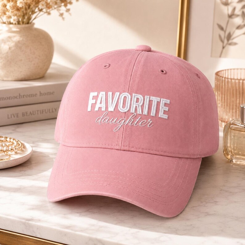 K&ouml;nnte beinhalten: Rosa Baseballkappe mit dem gestickten Text "FAVORITE daughter" in Wei&szlig;. Die Kappe hat einen gebogenen Schirm und eine abgerundete Oberseite. Der Hut ist aus einem weichen Stoff gefertigt.