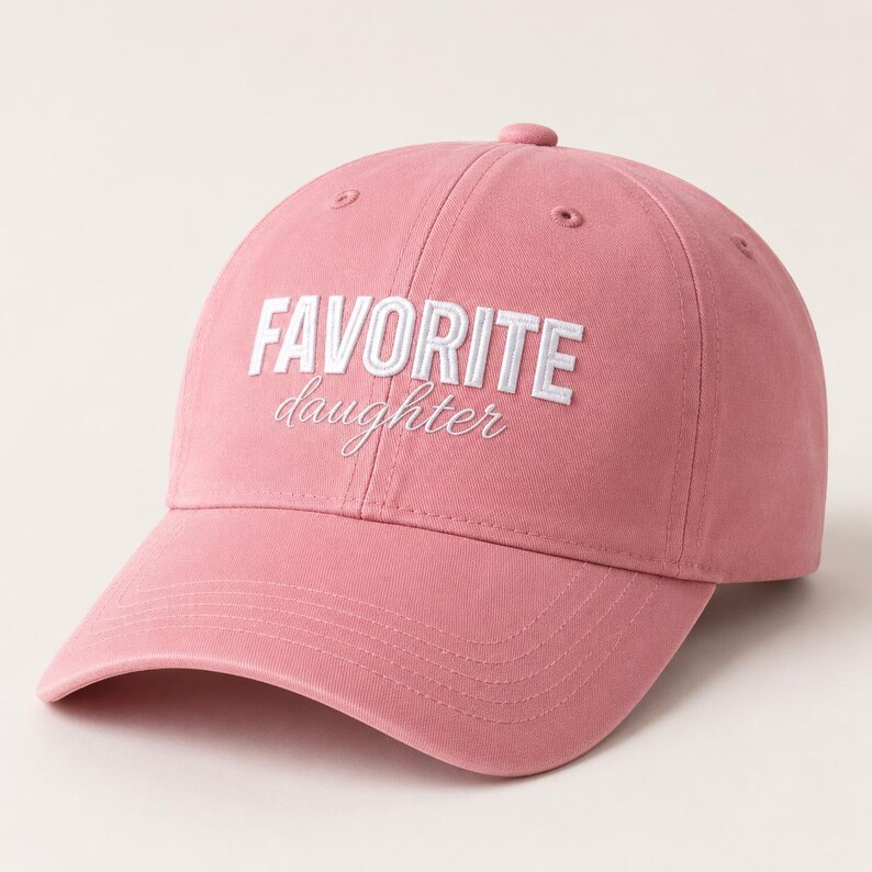 K&ouml;nnte beinhalten: Staubrosa Baseballkappe mit dem gestickten Text "FAVORITE daughter" in Wei&szlig;. Die Kappe hat einen gebogenen Schirm, einen Knopf oben und einen verstellbaren Riemen. Hergestellt aus einem weichen, strapazierf&auml;higen Stoff.