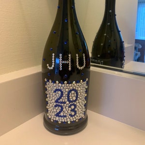 May include: A dark green glass bottle decorated with blue and clear rhinestones. The bottle has the letters 