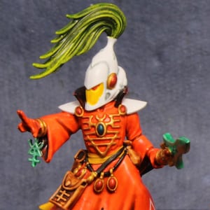 May include: Two painted miniature figurines featuring white helmets with tall green plumes, bright orange robes with white triangular symbols, and black boots. One figure holds a green sword, while the other holds a small green object.