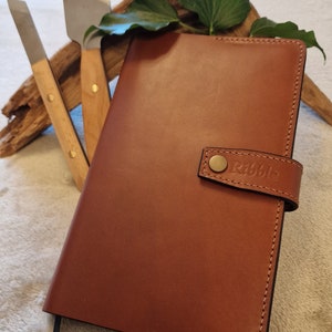 May include: A brown leather-bound journal with a black ribbon bookmark and a brass button closure. The journal has the word "Ribble" embossed on the front cover.