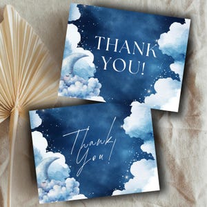 Może przedstawiać: Dwie granatowe kartki z podziękowaniami z akwarelowym wzorem śpiącego księżyca, chmur i gwiazd. Słowa "THANK YOU!" są napisane na jednej karcie na biało, a "Thank You!" w skrypcie na drugiej.