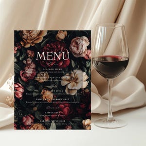 Może przedstawiać: Ciemne menu z motywem kwiatowym z napisem "MENU" w białym kolorze. Menu zawiera sałatkę z owoców morza, ravioli z parmezanem, stek z polędwicy wołowej, chrupiący filet z łososia, tartę cytrusową i ciasto jabłkowo-karmelowe.