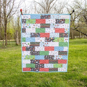 May include: A colourful patchwork quilt with a variety of patterns and colours, including red, green, blue and white. The quilt is hanging on a washing line outdoors.
