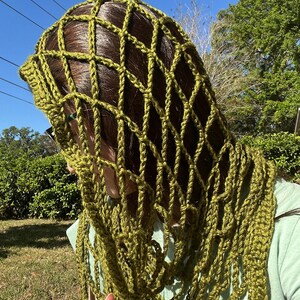 May include: A green crocheted shawl with a lacy pattern. The shawl is draped over a person's head and shoulders.