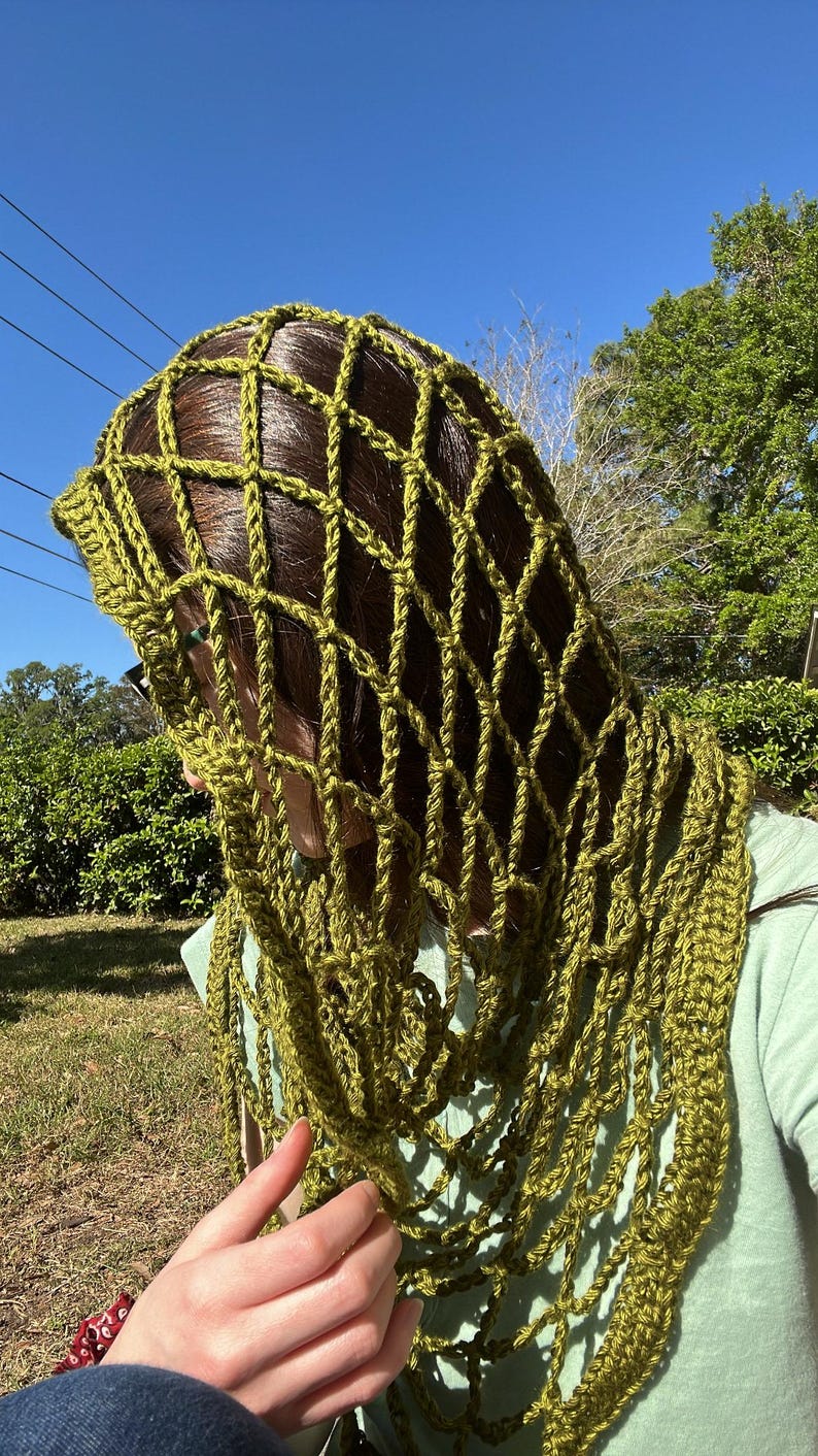 May include: A green crocheted shawl with a lacy pattern. The shawl is draped over a person's head and shoulders.