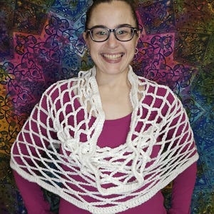 May include: A white crochet shawl with a net-like design. The shawl is draped around the shoulders of a person wearing a pink shirt.