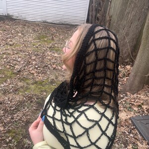 May include: A black crochet shawl with a web-like pattern. The shawl is draped over a person's shoulders and head.