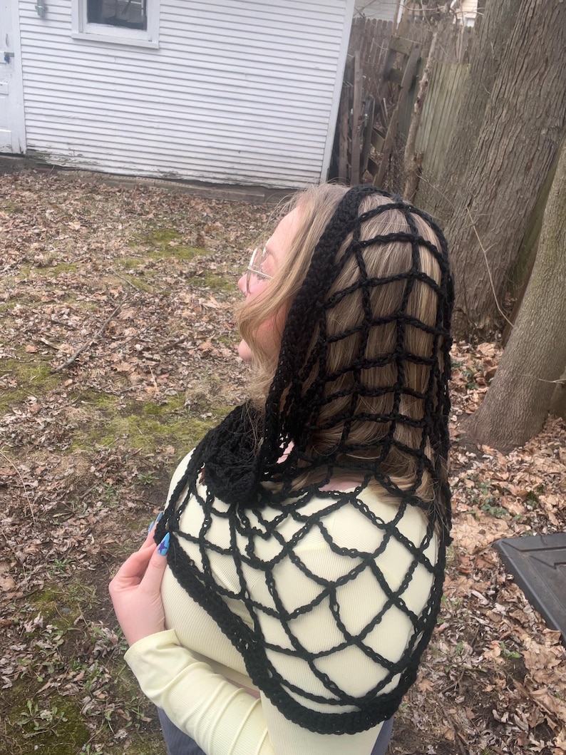 May include: A black crochet shawl with a web-like pattern. The shawl is draped over a person's shoulders and head.