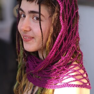 May include: A woman with long, brown hair with purple and green streaks wears a purple crocheted shawl over her head and shoulders. The shawl is a loose, open weave with a delicate pattern.
