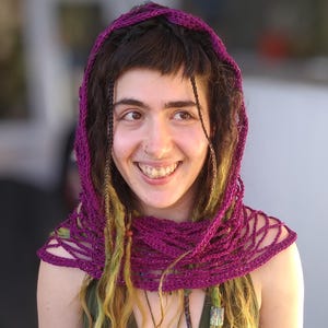 May include: A woman with long, braided hair wearing a purple crocheted shawl and a green shirt.