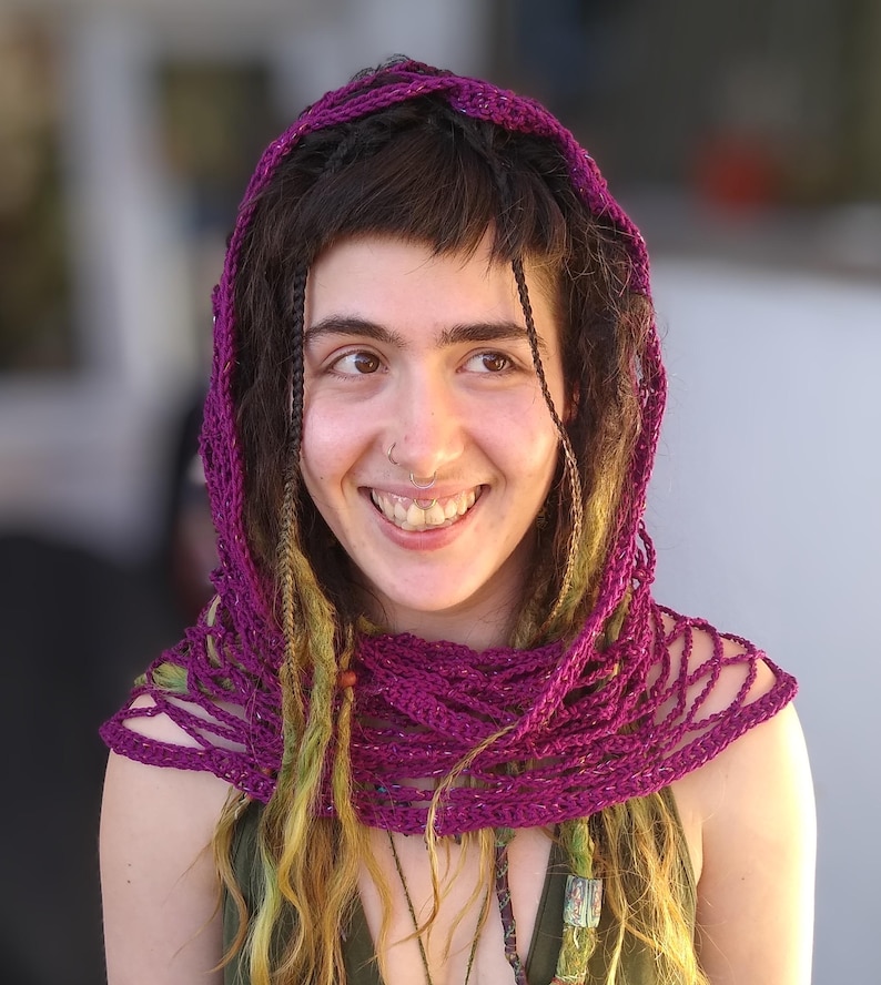 May include: A woman with long, braided hair wearing a purple crocheted shawl and a green shirt.
