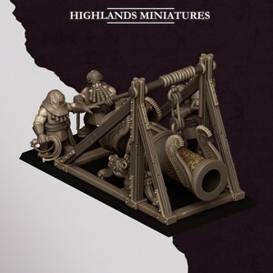 Puede incluir: Una pieza de artillería en miniatura con un gran cañón montado sobre un marco de madera, acompañado por tres figuras. El cañón tiene decoraciones ornamentales en forma de alas en la boca. El texto HIGHLANDS MINIATURES aparece arriba.