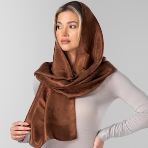 May include: A brown velvet scarf draped over the head and shoulders. The scarf is a rich, warm brown color and appears soft and luxurious. The fabric drapes elegantly, creating a stylish accessory.
