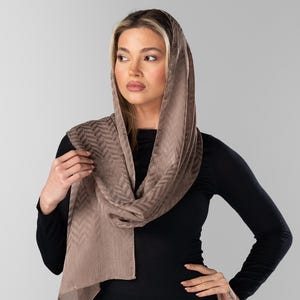 May include: A light brown scarf with a chevron pattern is draped over the head and shoulders. The scarf is made of a soft, flowing fabric. The person is wearing a black long-sleeved shirt.