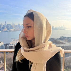 Puede incluir: Una mujer con un pañuelo beige con un horizonte urbano de fondo.