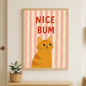 Peut inclure: Une affiche encadrée avec un chat tigré orange et le texte "NICE BUM" en rouge. Le fond présente des rayures verticales roses et crème. L'œuvre est affichée sur une table en bois clair, idéale pour la décoration intérieure.