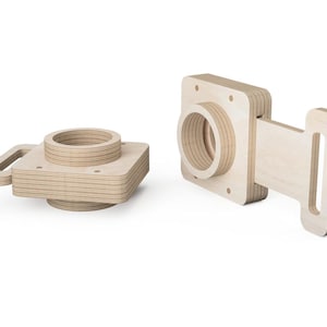 Puede incluir: Dos soportes de cámara de madera clara. Uno tiene un asa y una abertura circular. El otro tiene forma cuadrada con una abertura circular y un asa rectangular.