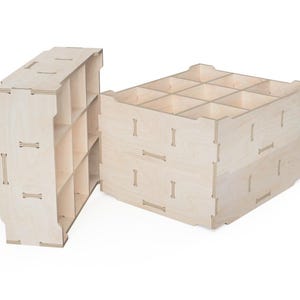 Peut inclure: Deux cubes de rangement en bois non finis avec plusieurs compartiments. Les cubes sont en bois clair et présentent des joints imbriqués. Un cube est partiellement ouvert, révélant les étagères intérieures.