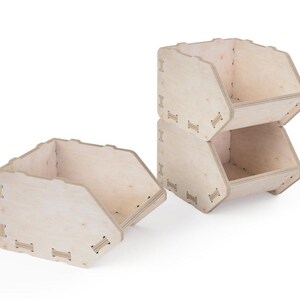 May include: Three light-coloured wooden storage bins. Two bins are stacked, and one is separate. The bins have a unique shape with angled sides and are assembled with small wooden connectors. The bins are empty and sit on a white background.