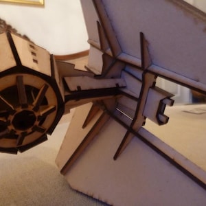 May include: A wooden model of a spaceship with a detailed cockpit and a large, round engine. The model is made of laser-cut wood and is assembled with precision.