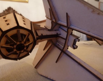 May include: A wooden model of a spaceship with a detailed cockpit and a large, round engine. The model is made of laser-cut wood and is assembled with precision.
