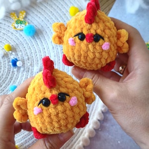 May include: Two handmade, plush, yellow chicken toys with red combs, feet, and beaks, and pink cheeks. The chickens have black eyes and small, round bodies. The toys are held in a person's hands.