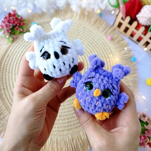 May include: Two handmade crochet owl figurines. One is white with black and brown details, the other is purple with orange and green accents. The owls have large, expressive eyes and are made with soft, textured yarn. They are displayed against a neutral background.