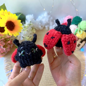 May include: Two small, handmade crochet ladybug plushies made from soft black and red yarn. Each plush features a rounded black body, two black antennae, and vibrant red wings with small black embroidered spots. One ladybug has visible green eyes.
