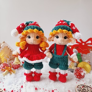May include: Two crocheted elf dolls with green and red outfits. The elf on the left is wearing a red dress with white trim and a green hat. The elf on the right is wearing a green jumpsuit with a red hat.