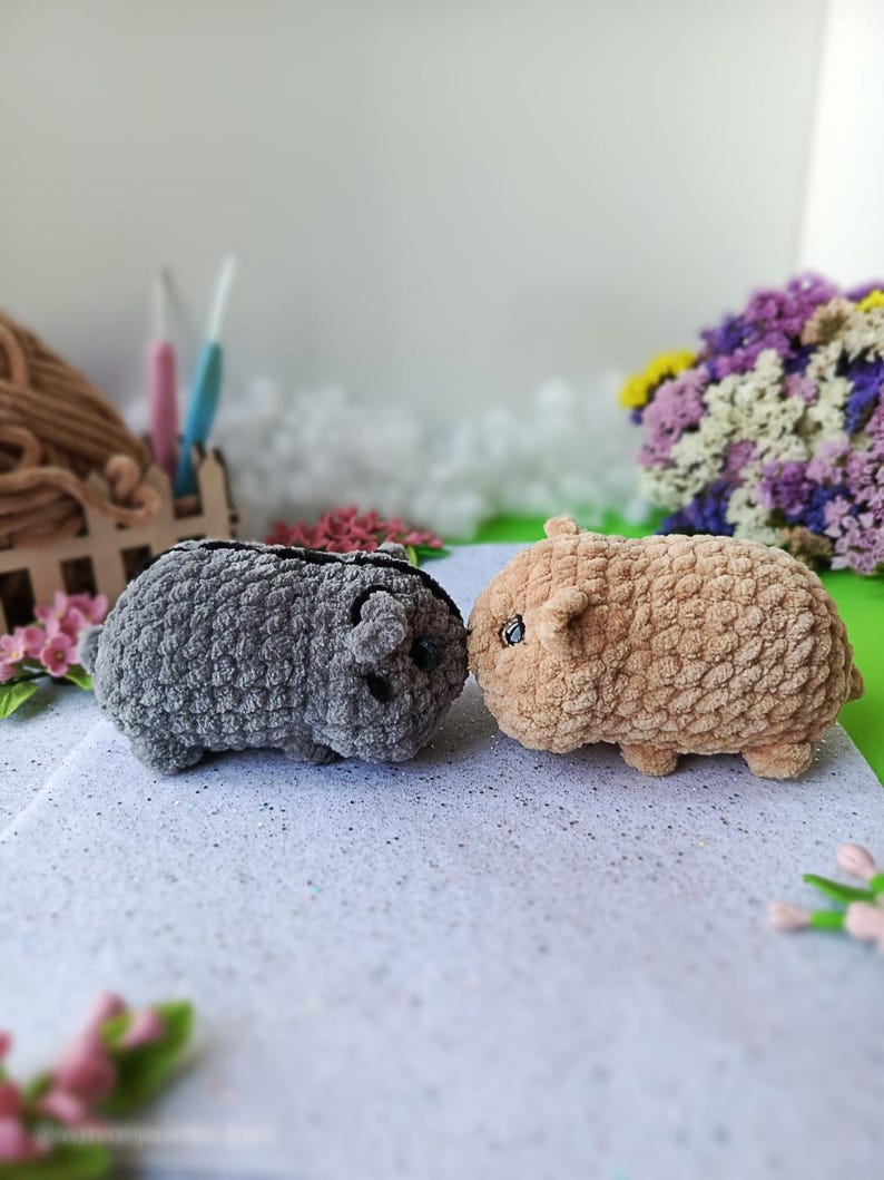 May include: Two handmade crochet guinea pig toys. One is gray, the other is tan. Both have small ears and black eyes. The toys are made with a soft, textured yarn and are sitting on a white surface.