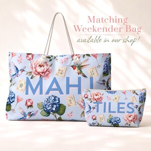 May include: A light blue tote bag and a matching zippered pouch featuring a floral pattern with hummingbirds, mahjong tiles, and cocktail glasses. The tote bag displays the text MAH and the pouch displays the text TILES in large blue letters.