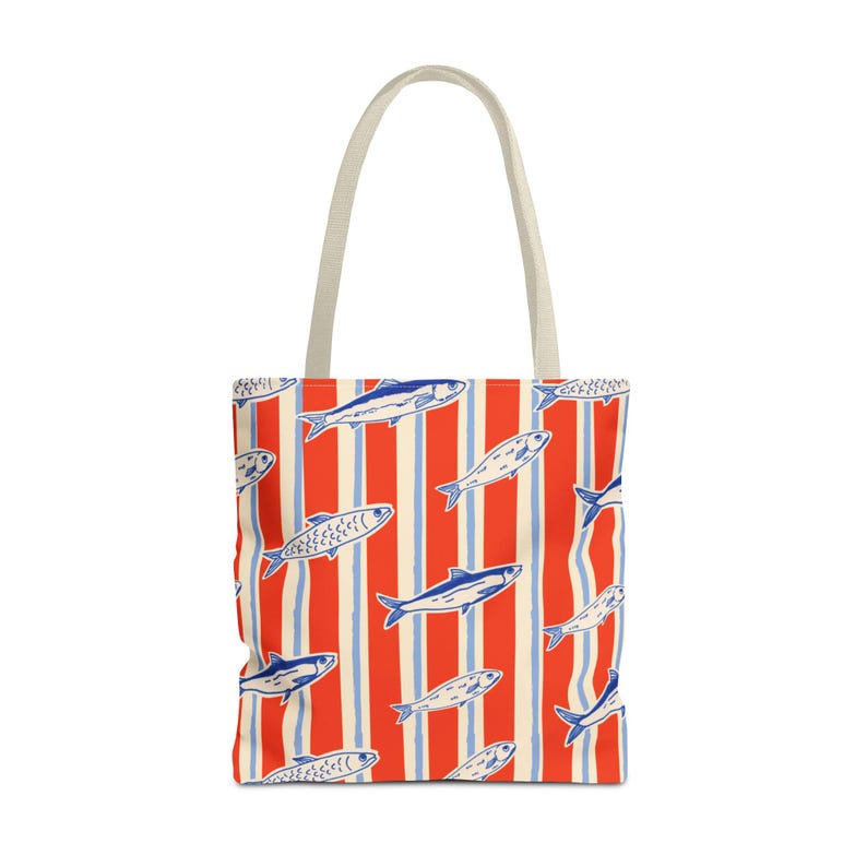 May include: A tote bag with a repeating pattern of blue and white fish on a red and white striped background. The bag has a cream-colored handle and is made of a durable fabric.